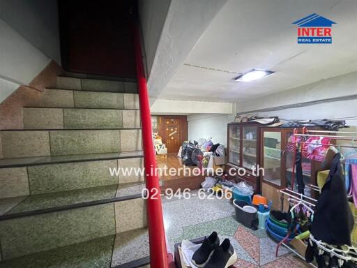 Interior view of a cluttered building entrance with staircase and storage area