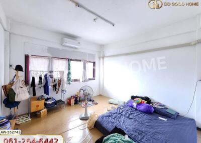 A bedroom with scattered items, an air conditioner, window, fan, bed with blue bedding, and various storage items.