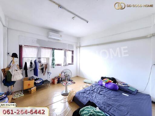A bedroom with scattered items, an air conditioner, window, fan, bed with blue bedding, and various storage items.