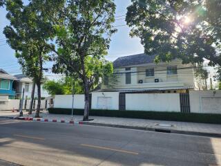 Exterior view of a two-story house with a fenced yard and trees on a sunny day