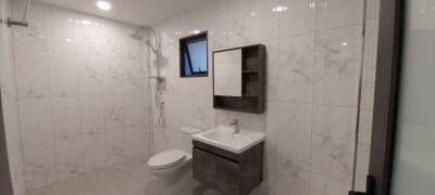 Modern bathroom with white marble tiles, wall-mounted sink, and spacious shower area