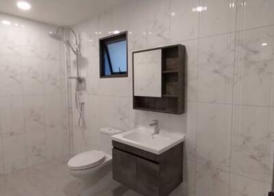 Modern bathroom with white marble tiles, wall-mounted sink, and spacious shower area