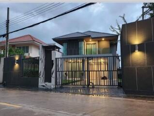 Modern two-story house with illuminated facade and secure gate during twilight