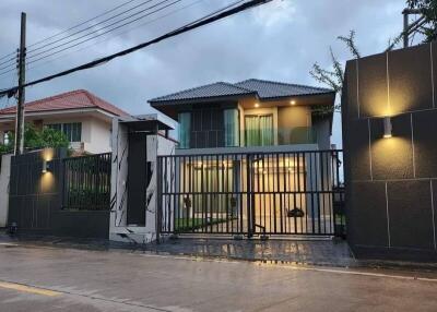 Modern two-story house with illuminated facade and secure gate during twilight