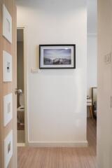 Modern hallway interior with framed artwork, wooden flooring, and view into bathroom