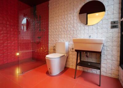 Modern bathroom with red and white tiles, featuring a stylish sink, toilet, and shower area