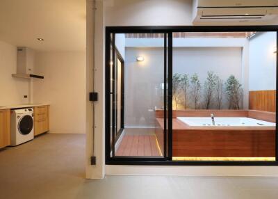 Modern kitchen leading to an elegant outdoor bathtub surrounded by wooden decks and lush greenery