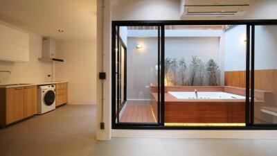 Modern kitchen leading to an elegant outdoor bathtub surrounded by wooden decks and lush greenery