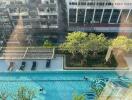 Aerial view of a residential building complex with an outdoor swimming pool surrounded by lush greenery