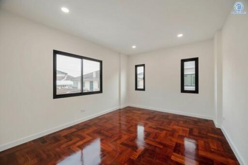 Spacious well-lit bedroom with polished hardwood floors and multiple windows