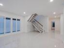 Spacious white-themed living room with large windows and an elegant staircase