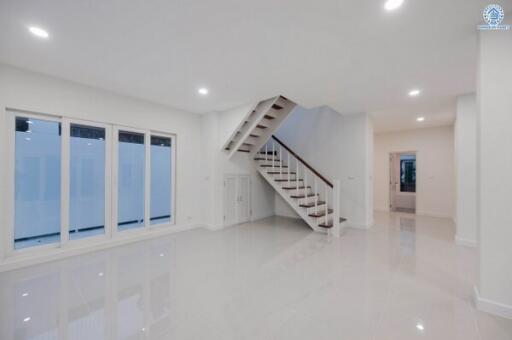 Spacious white-themed living room with large windows and an elegant staircase