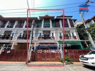 Exterior view of a red two-story residential building with balconies and a wooden fence