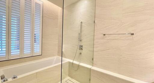 Modern bathroom with bathtub and shower combination, light marble walls and plantation shutters