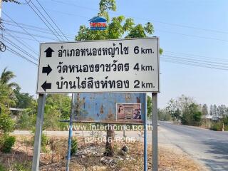 Street sign showing directions to various locations with a blurred real estate advertisement board in the background