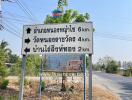 Street sign showing directions to various locations with a blurred real estate advertisement board in the background