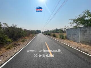 Suburban road with clear skies and surrounding vegetation, leading to potential residential or commercial areas