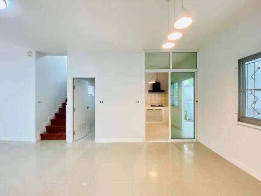 Spacious living room with white tiled flooring, staircase and glass door leading to the kitchen