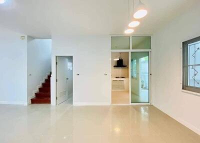 Spacious living room with white tiled flooring, staircase and glass door leading to the kitchen