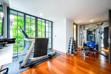 Modern home gym with large windows, treadmill, weightlifting equipment, and wooden flooring