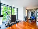 Modern home gym with large windows, treadmill, weightlifting equipment, and wooden flooring