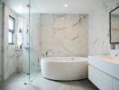 Luxurious modern bathroom with marble tiles, large bathtub, and glass shower