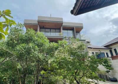 Exterior view of a modern multi-story building surrounded by lush greenery under a cloudy sky