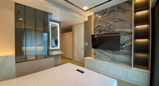 Elegant bedroom with modern aesthetic featuring a detailed marble wall, sleek built-in storage and a large window