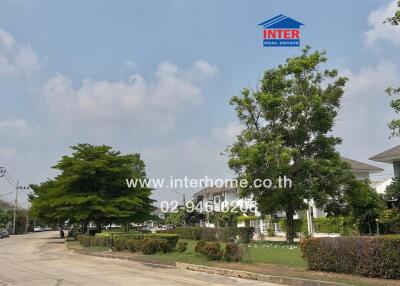 View of a residential street with houses and lush greenery under a clear sky