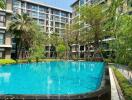 Luxurious residential building with large swimming pool surrounded by lush greenery