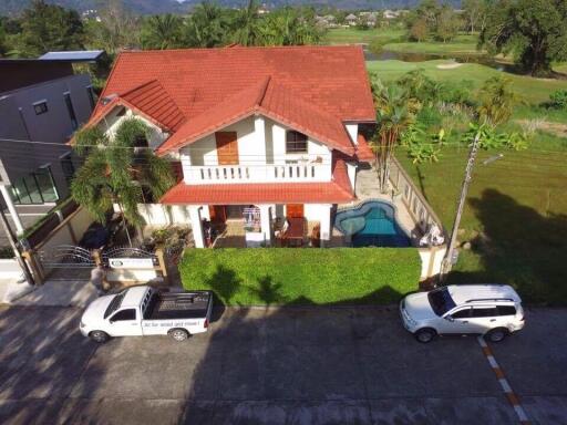 Aerial view of a two-story house with a red roof, featuring a swimming pool and parked cars