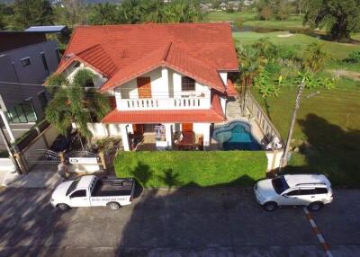Aerial view of a two-story house with a red roof, featuring a swimming pool and parked cars