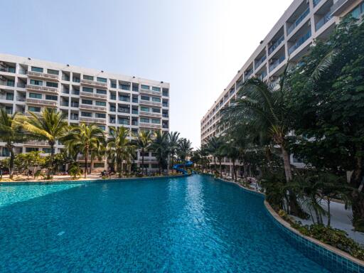 Outdoor swimming pool surrounded by lush greenery with residential buildings in background