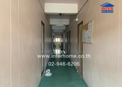 Long narrow corridor in a building with green tiled floor and bulletin board