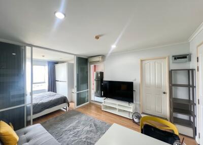 Spacious bedroom with integrated living space featuring large bed, modern TV, and ample lighting