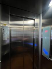 Interior of a modern elevator with reflective metal walls and a digital control panel