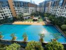 Aerial view of a luxurious residential building complex with a large swimming pool and lush greenery