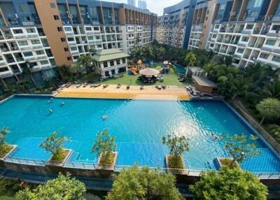 Luxurious condominium complex with large swimming pool surrounded by lush greenery and apartment buildings