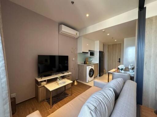 Modern compact living room with integrated kitchen appliances, bright lighting, and stylish furniture