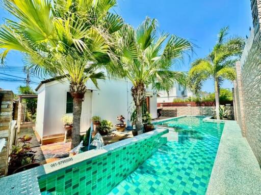 Luxurious backyard with a large swimming pool surrounded by palm trees and a well-maintained garden, leading to a modern house
