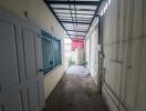 Narrow exterior corridor of a house with a partially covered ceiling, water tank, and a large window