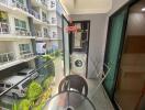 Compact balcony with washing machine and seating area in an apartment complex