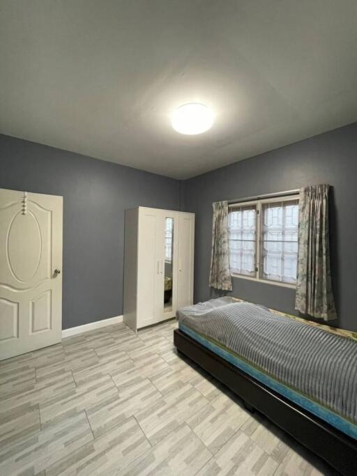 Spacious bedroom with grey walls, large window with curtains and a single bed