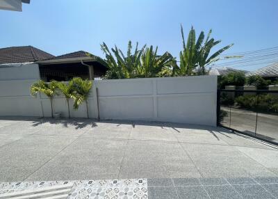 Sunlit exterior view of a residential property showing a high privacy fence and lush greenery
