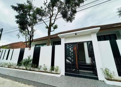 Modern single-story house with white exterior and stylish black gate surrounded by green trees