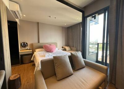 Modern bedroom with ample natural light, featuring a comfortable bed, workspace, and a stylish seating area