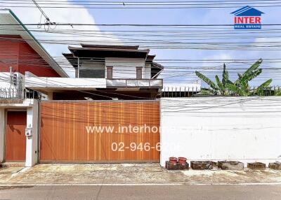 Exterior view of a two-story residential building with a large metal gate and surrounding wall