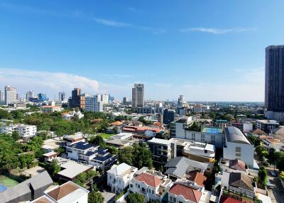 Panoramic cityscape view from a high-rise building showing a mix of residential houses, high-rise apartments, and commercial buildings under a clear blue sky