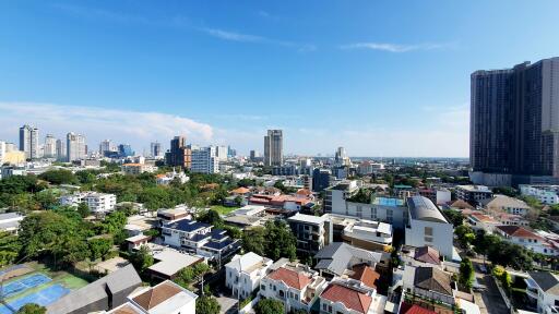 Panoramic cityscape view from a high-rise building showing a mix of residential houses, high-rise apartments, and commercial buildings under a clear blue sky