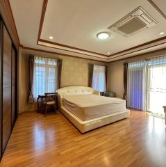 Spacious bedroom with wooden flooring, a large bed, wooden furniture, large windows with transparent drapes, and ceiling lighting